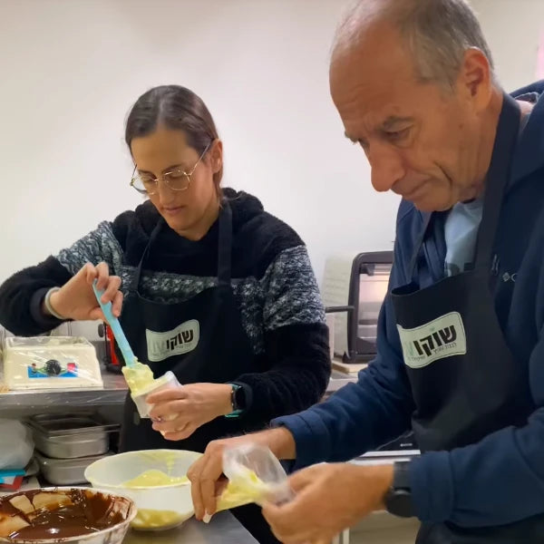 משתתפים בסדנת שוקולד למבוגרים של שוקוליב מכינים ומעבירים קרם מילוי לשקיות זילוף בעבודת יד