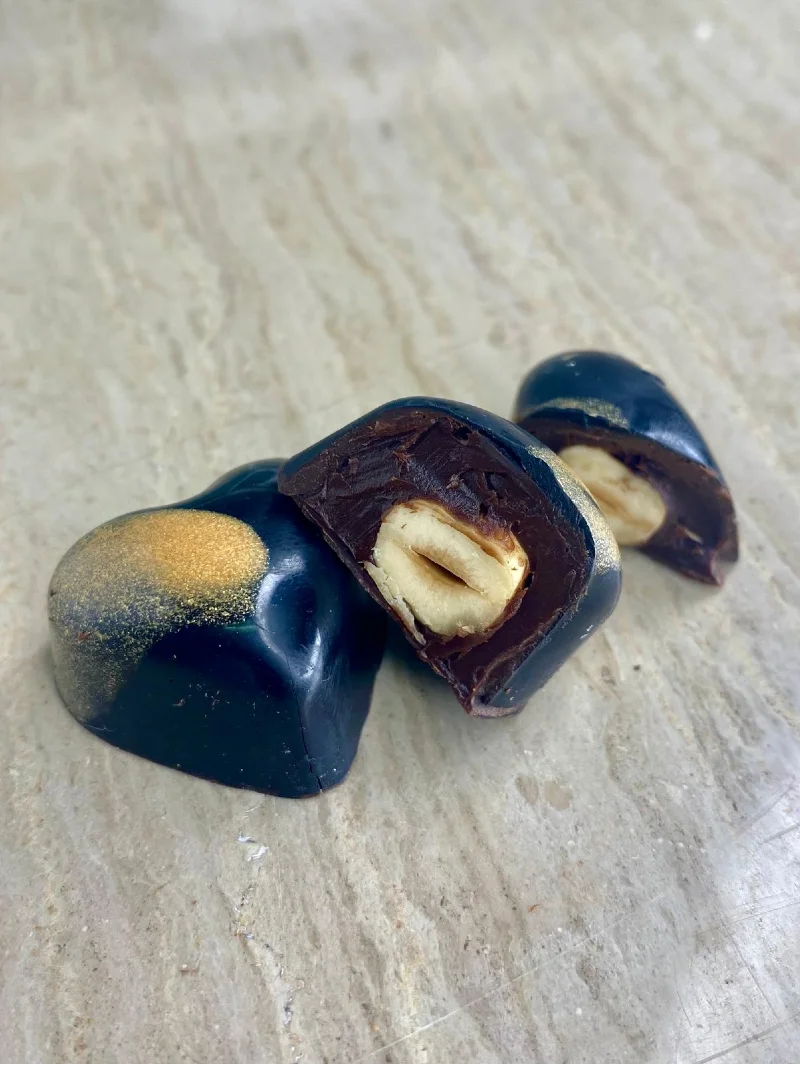 תקריב של פרלין שוקולד מריר איכותי חצוי, החושף מילוי קרם עשיר ואגוז לוז שלם וקלוי, מתוצרת שוקוליב