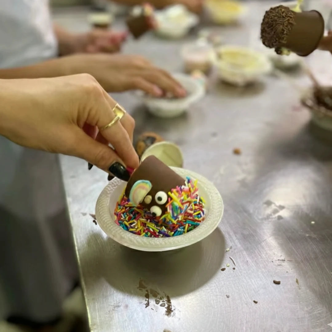 משתתפים בסדנת שוקולד של שוקוליב מקשטים קינוחי שוקולד על מקל עם סוכריות צבעוניות וזילופים.