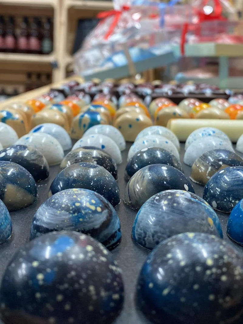 שורות של פרלינים צבעוניים בעבודת יד במראה גלקסיה וחלל מתוך קולקציית השוקולד של שוקוליב