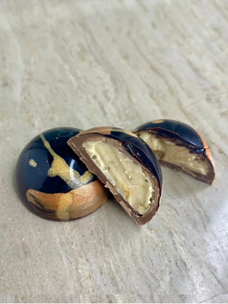 תקריב של פרלין שוקולד מעוצב וחצוי עם מילוי קרם גנאש בהיר ועשיר, תוצרת סדנת השוקולד שוקוליב